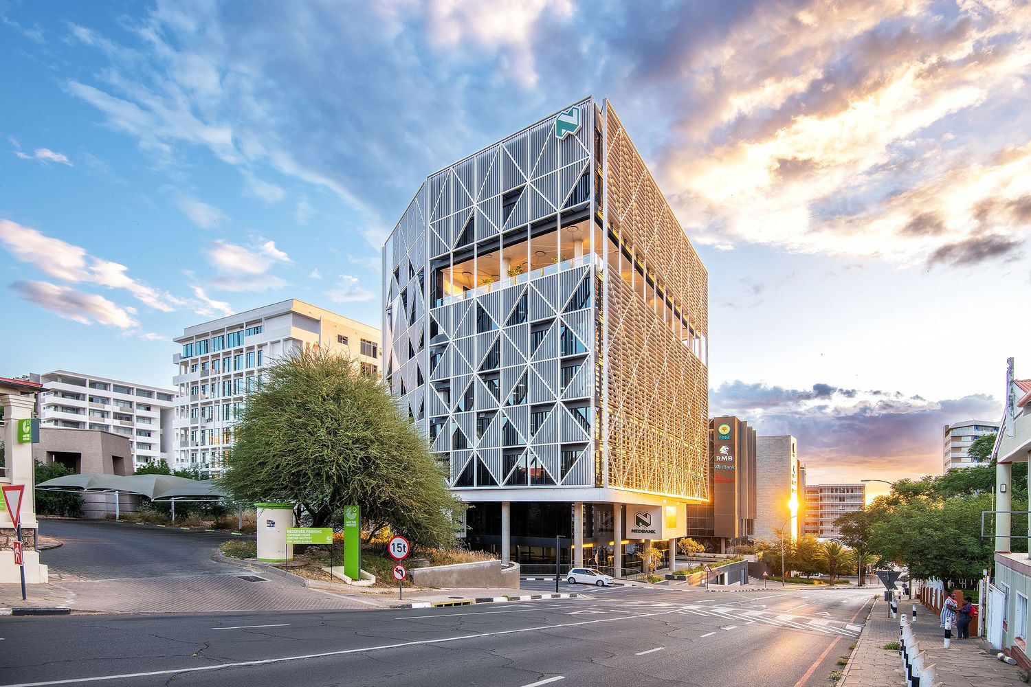 Striking modern office tower with geometric facade and warm sunset sky in Sandton business district.