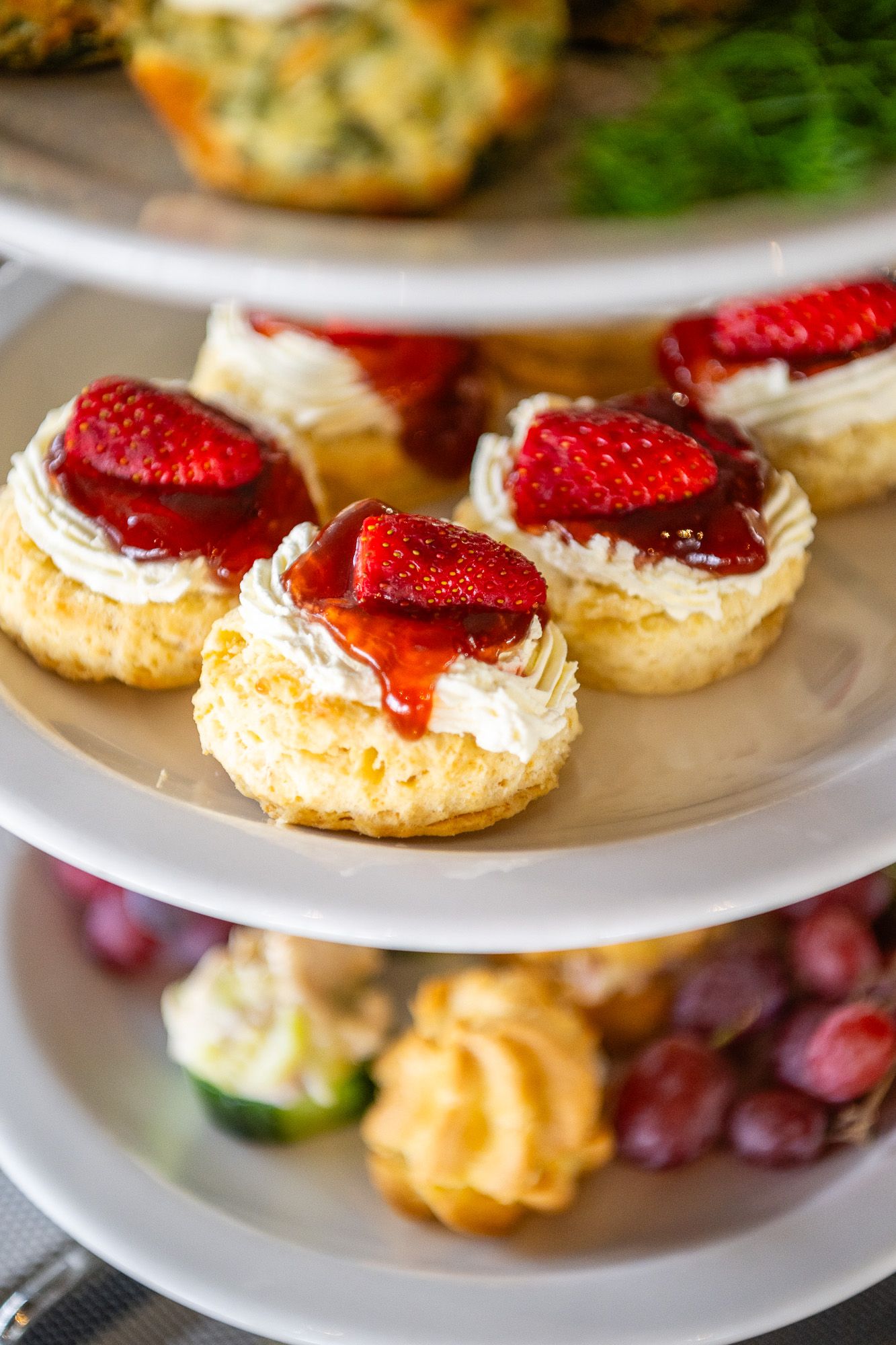 Elegant tiered dessert stand with strawberry cream tarts topped with jam, grapes, and pastries at a catered event.
