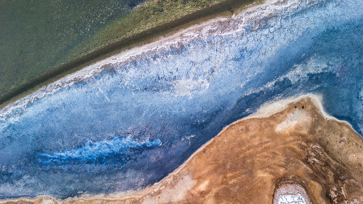 Aerial view of a stunning coastal landscape with blue icy patterns meeting sandy brown shores and turquoise water.