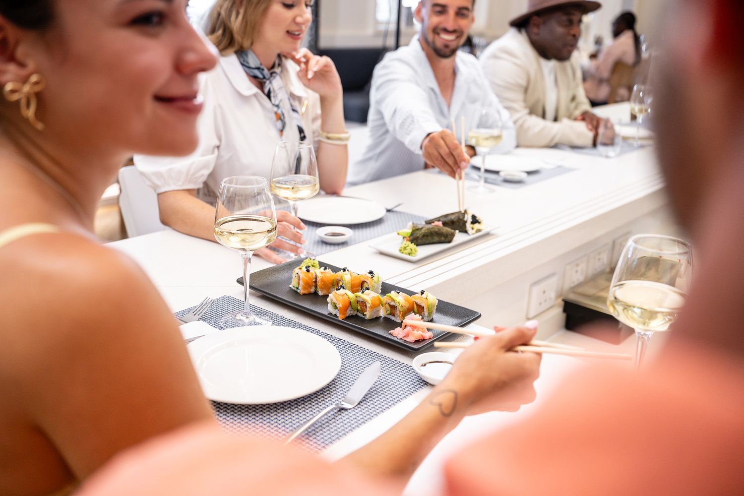 Group of friends enjoying sushi and white wine at an elegant restaurant dining table.