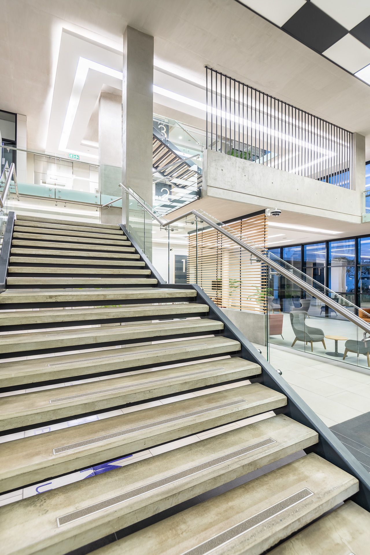 Modern building interior featuring wide marble staircase with glass railings, open atrium, and contemporary lighting design.