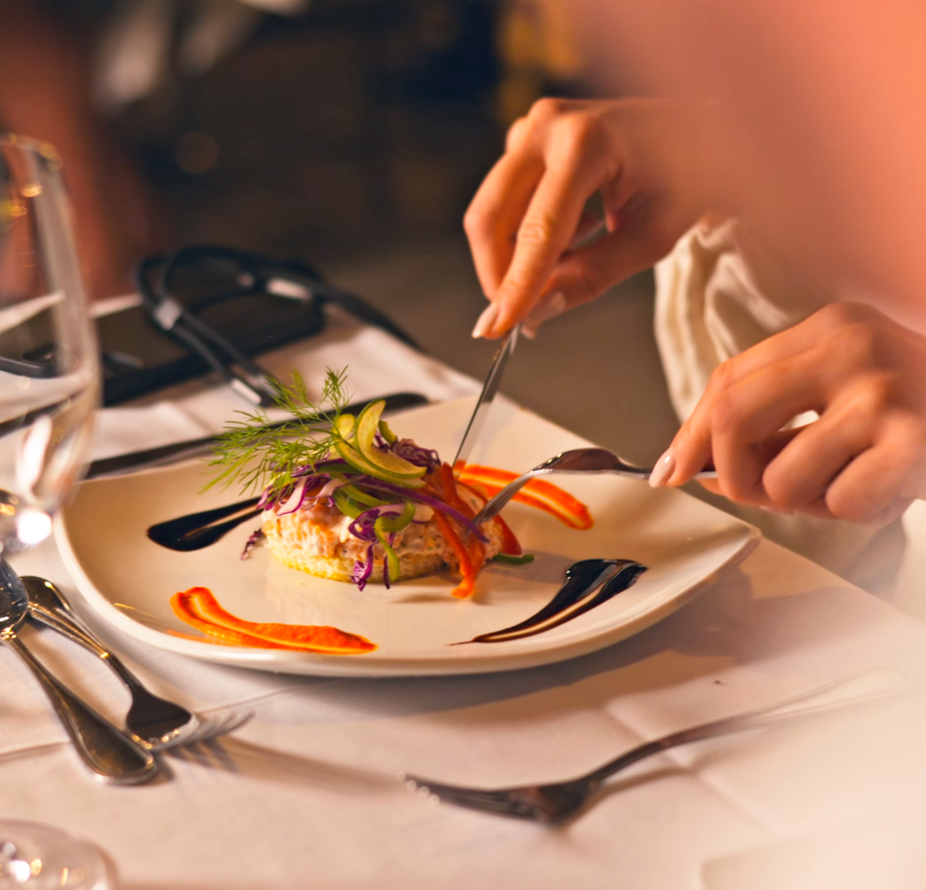 Person cutting into an elegantly plated gourmet dish with colorful vegetables at a fine dining restaurant.