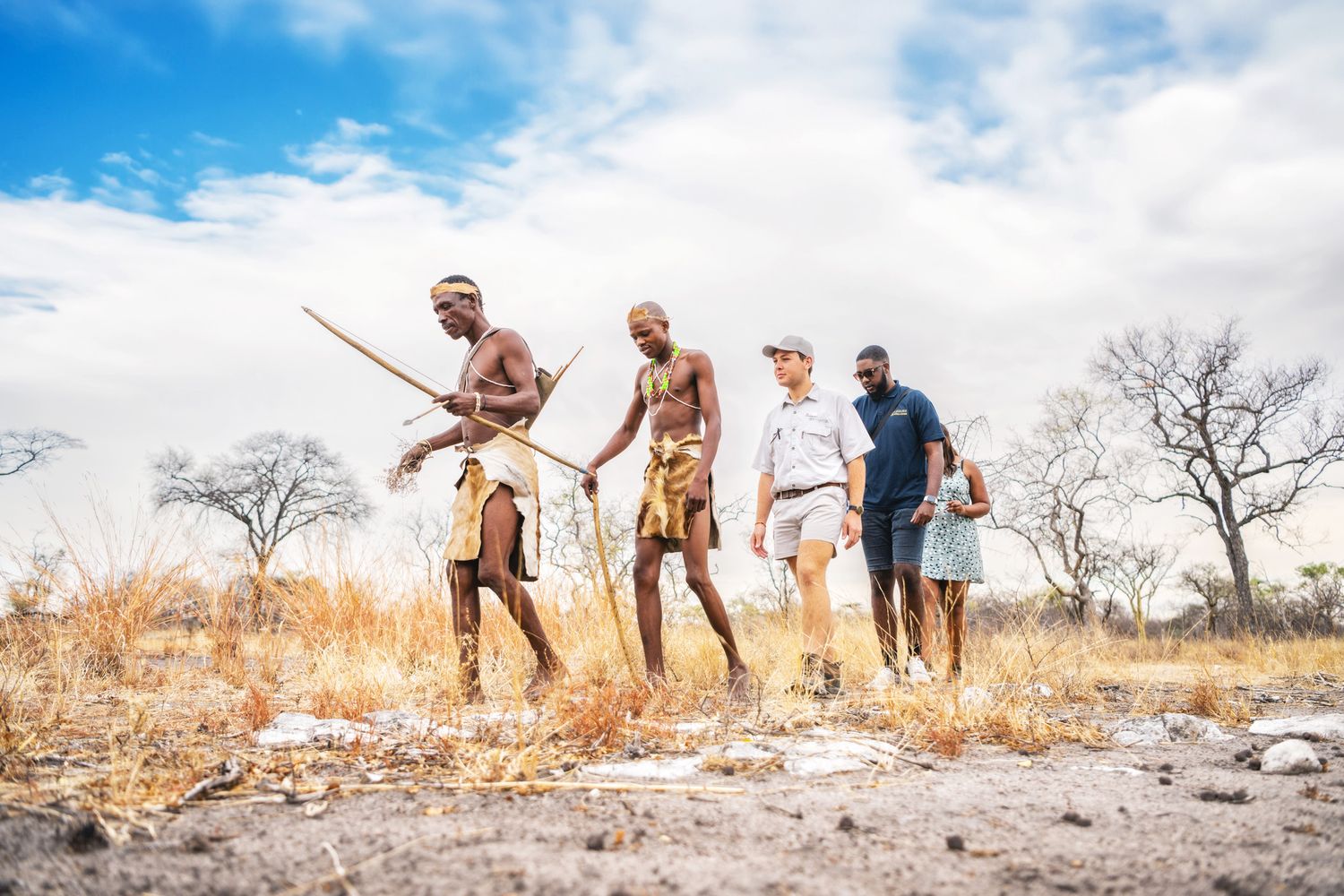 San Bushmen guides lead tourists on a traditional bush walk in the arid African savanna landscape.