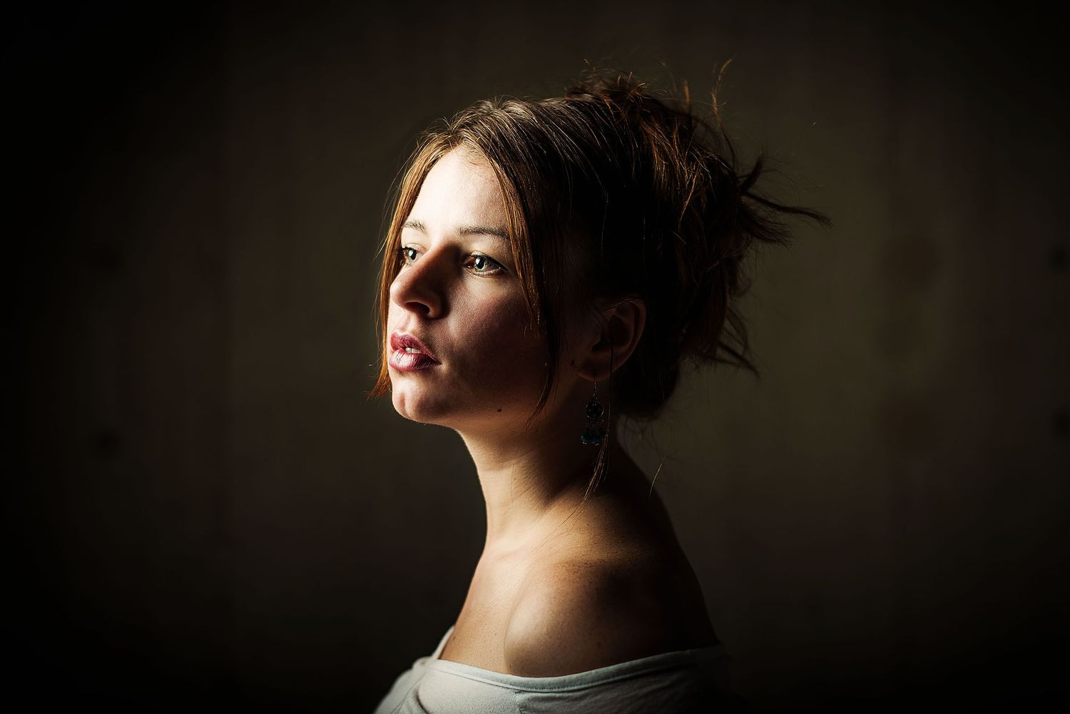 Dramatic portrait of a young woman with upswept hair against a dark background, lit by moody side lighting.
