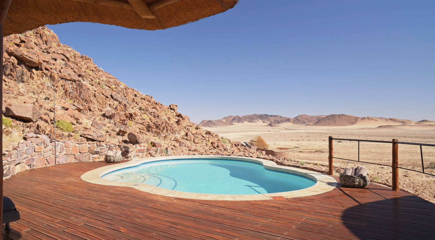 A small pool on a wooden deck surrounded by rocky desert mountains under a clear sky in Namibia.