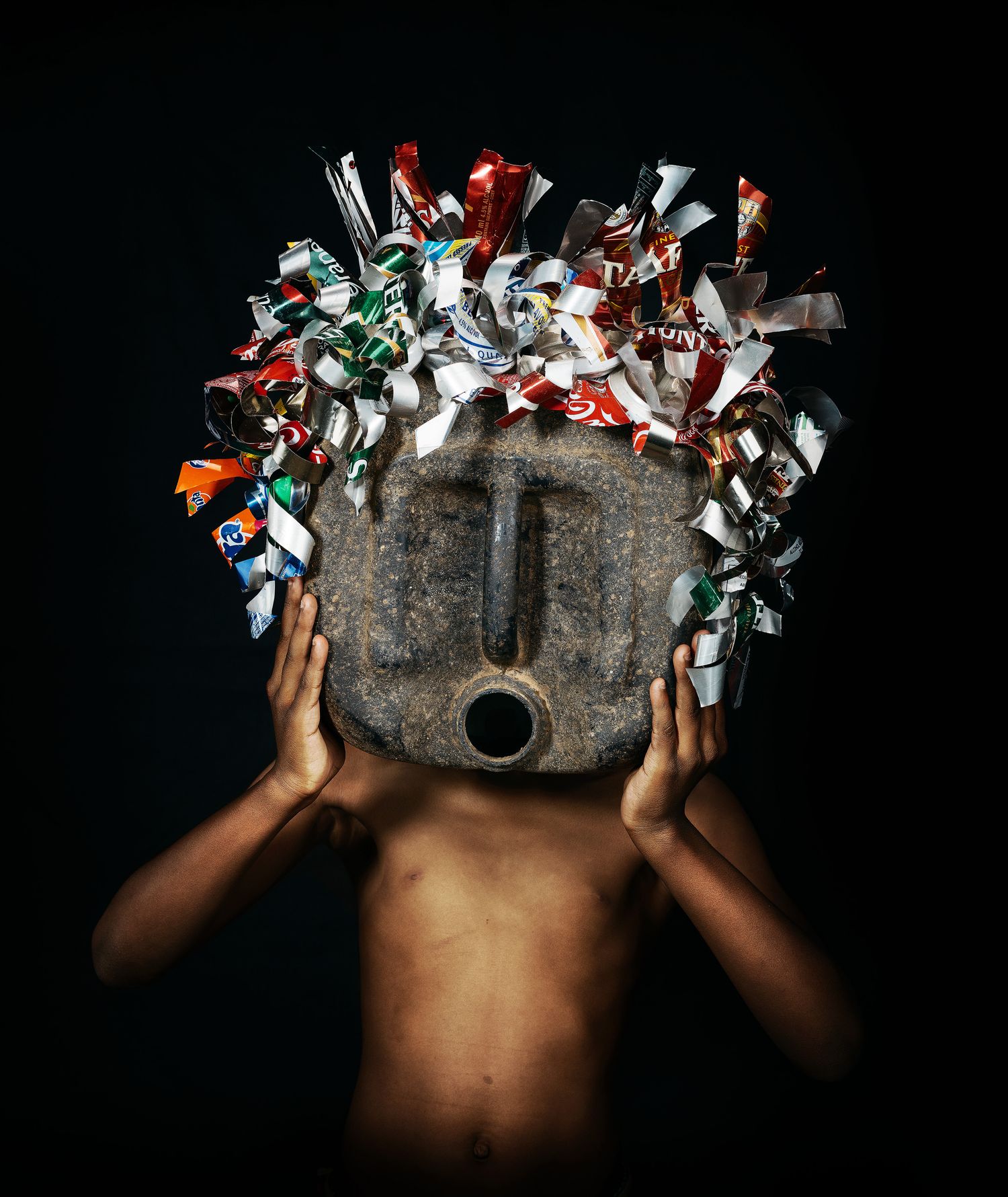 Person holding a traditional African mask decorated with colorful candy wrappers against a dark background.