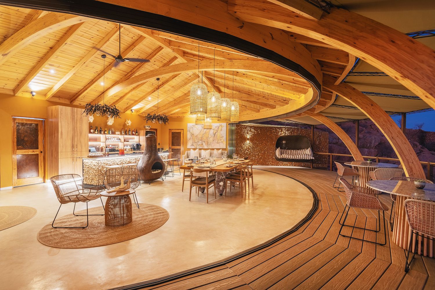 Stunning curved wooden interior of a luxury lodge with warm lighting, dining area, and sweeping timber arch design.