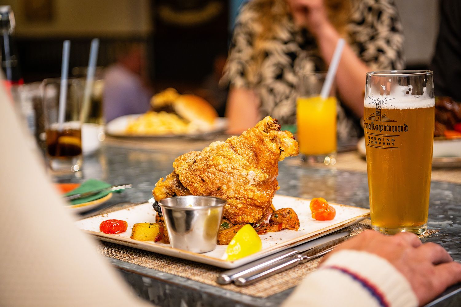 Crispy fried chicken served on a white plate with dipping sauce beside a cold beer at a restaurant bar.