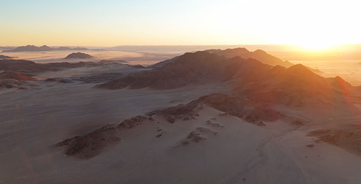 Aerial view of desert mountains at golden sunset with misty valleys below.