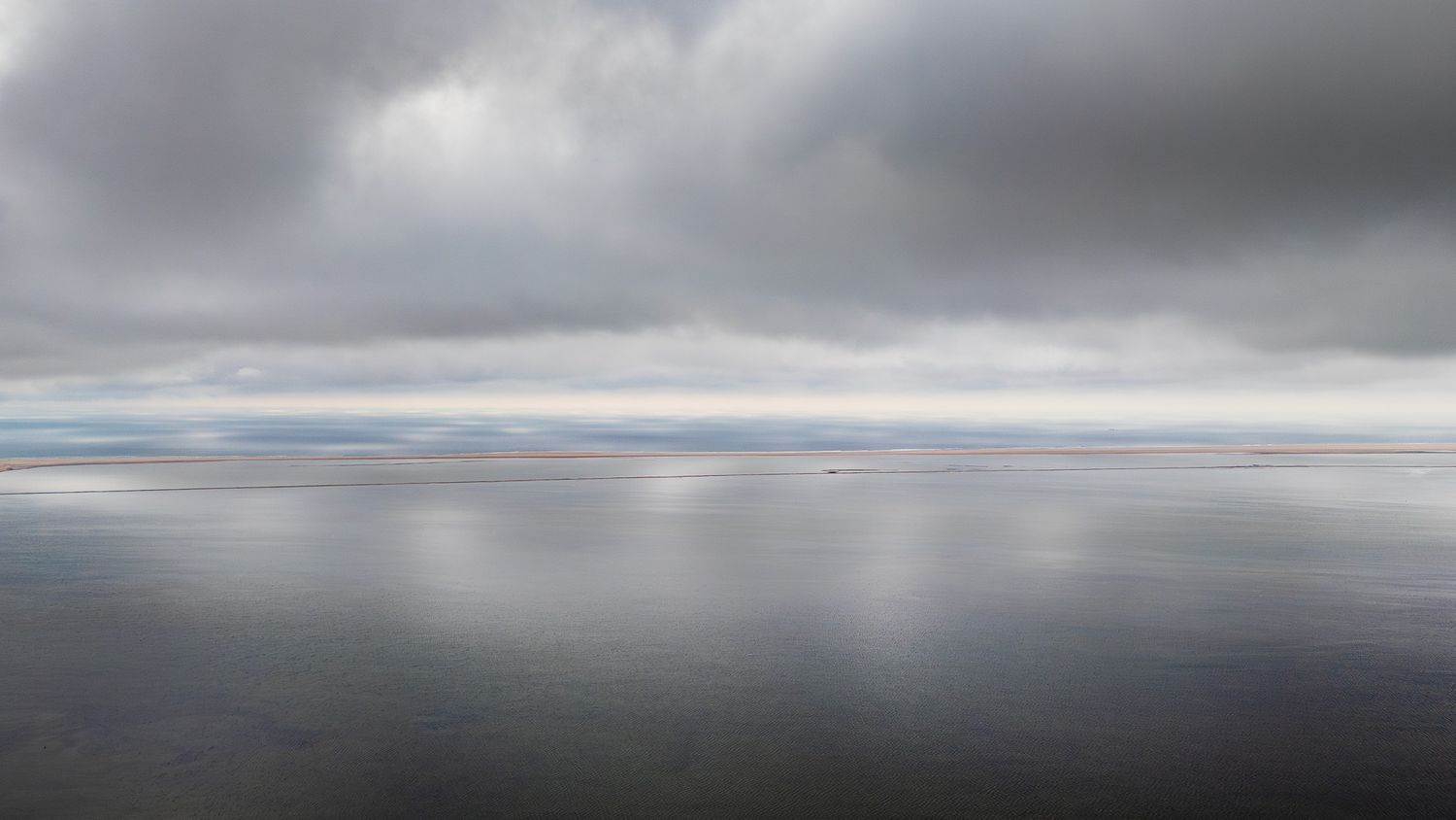 Calm reflective ocean water under overcast gray cloudy sky creating a serene minimalist seascape.