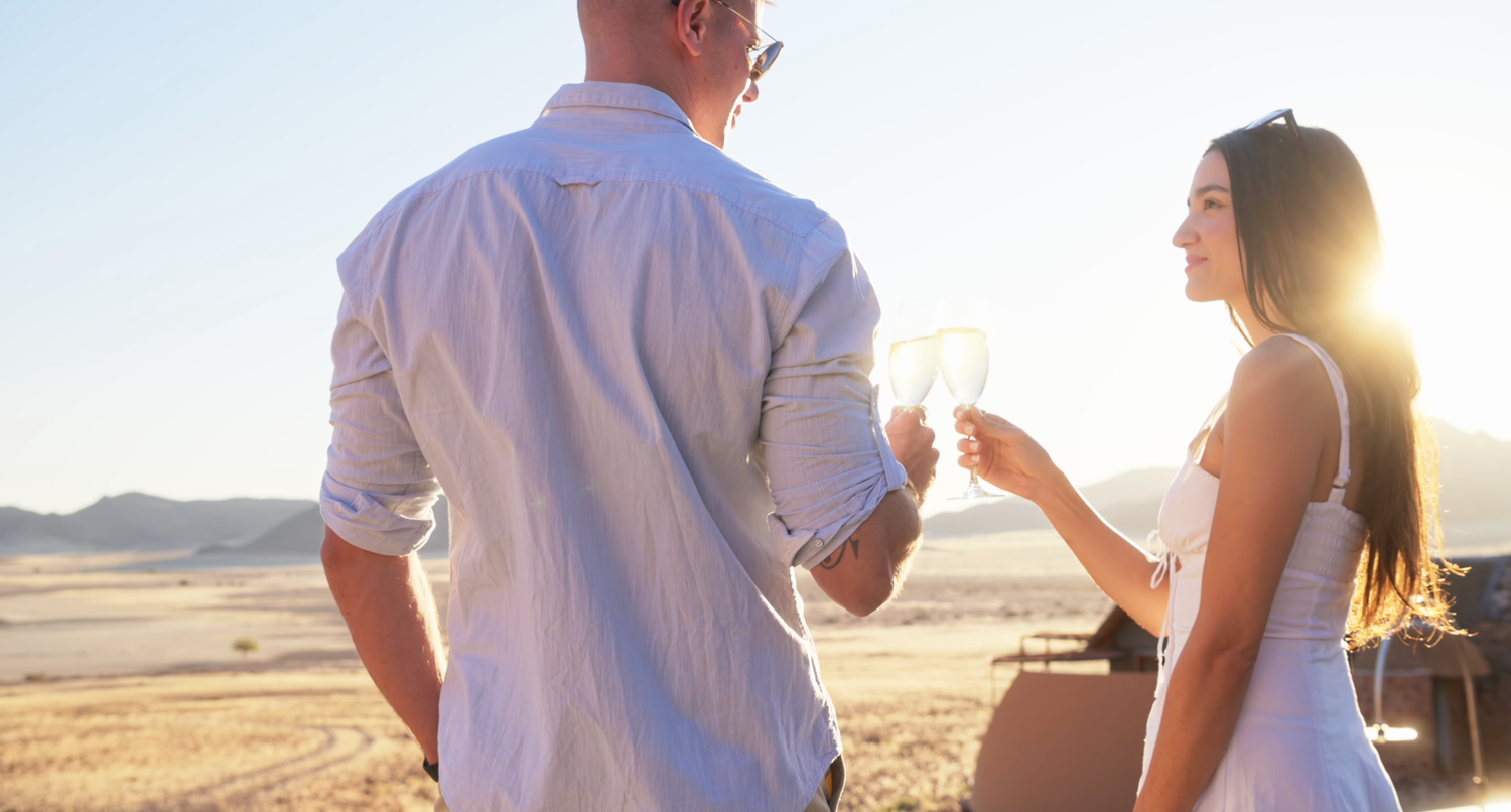 Couple toasting champagne glasses at sunset in a desert landscape, romantic outdoor celebration.