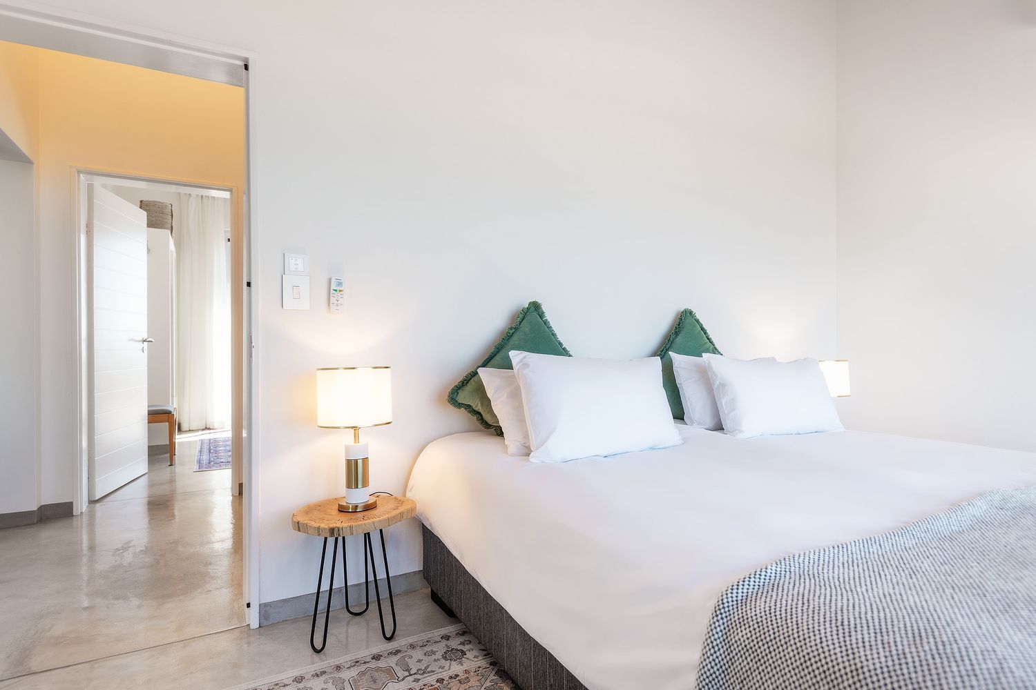 Bright modern bedroom with king bed, white bedding, green accent pillows, bedside lamp, and open door to hallway.