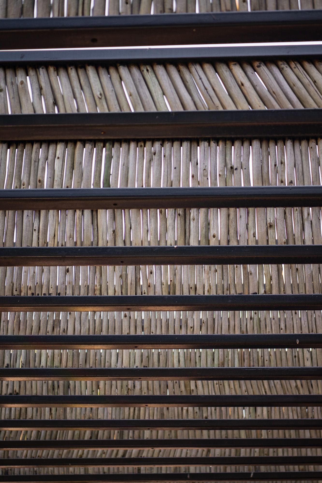 Close-up view of wooden slats arranged diagonally between dark metal horizontal bars, creating a geometric pattern.