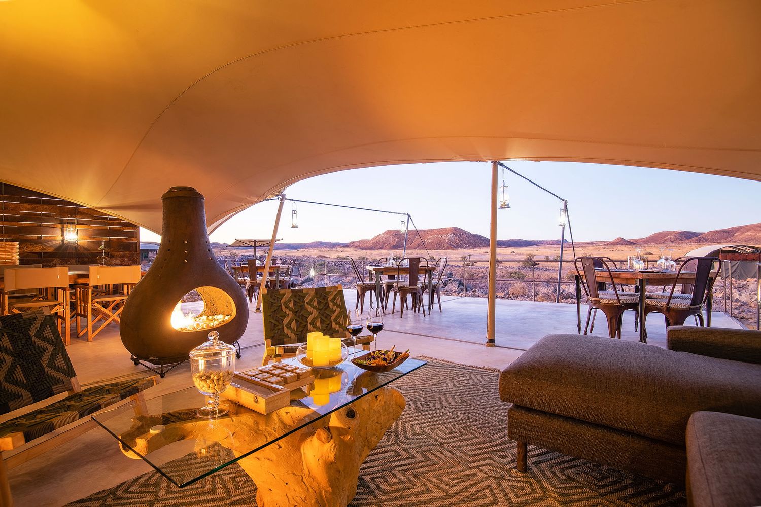 Luxury glamping tent with fireplace, glass coffee table, and panoramic desert views at golden hour.
