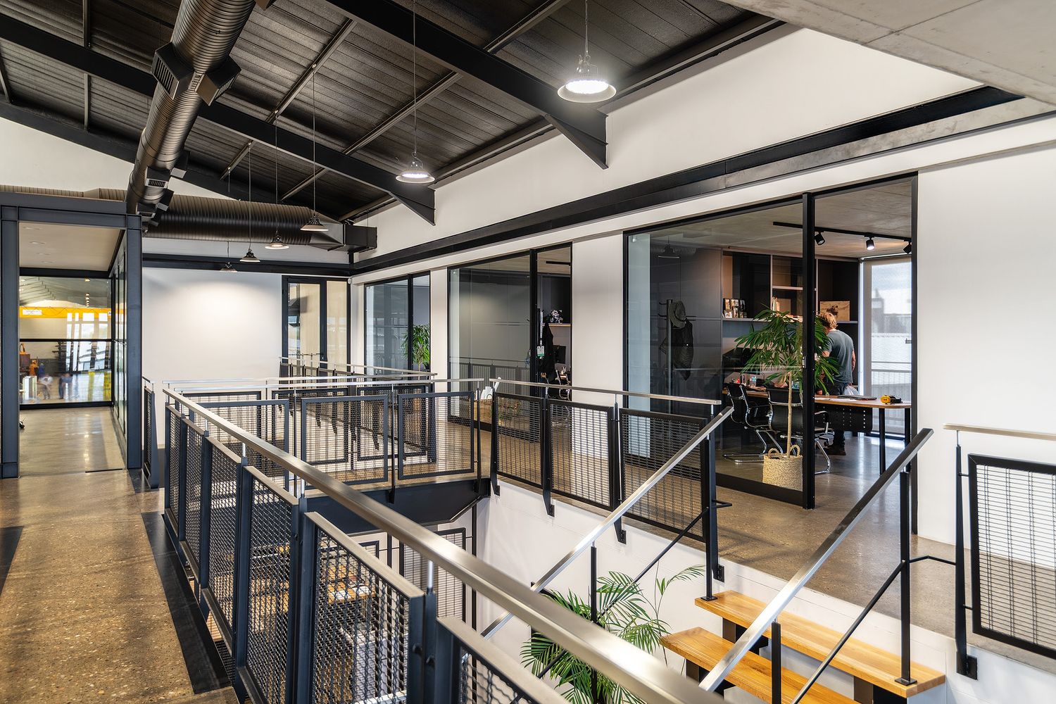 Modern industrial office mezzanine with black steel railings, glass partition walls, and open workspace on polished concrete floors.