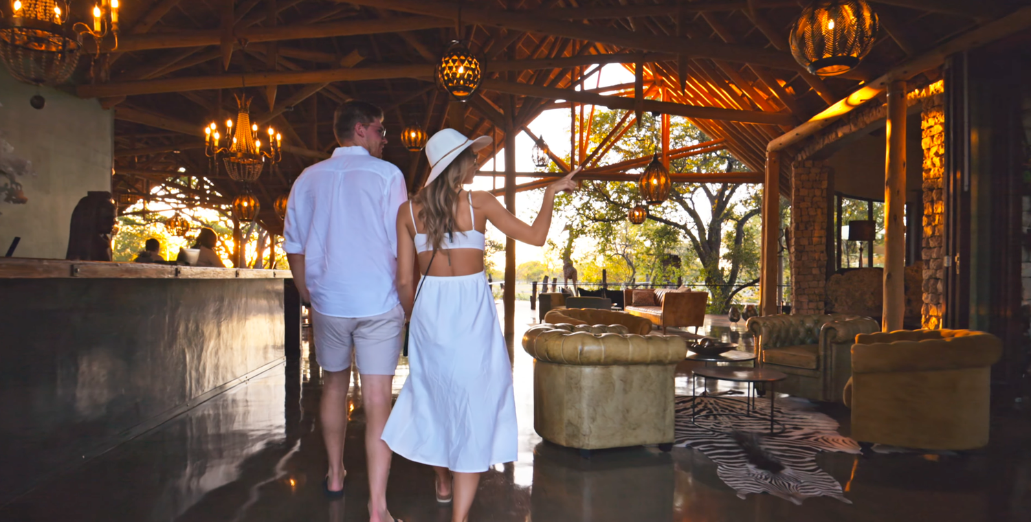 Couple walking hand-in-hand through a luxurious safari lodge lobby with warm lighting and elegant decor.