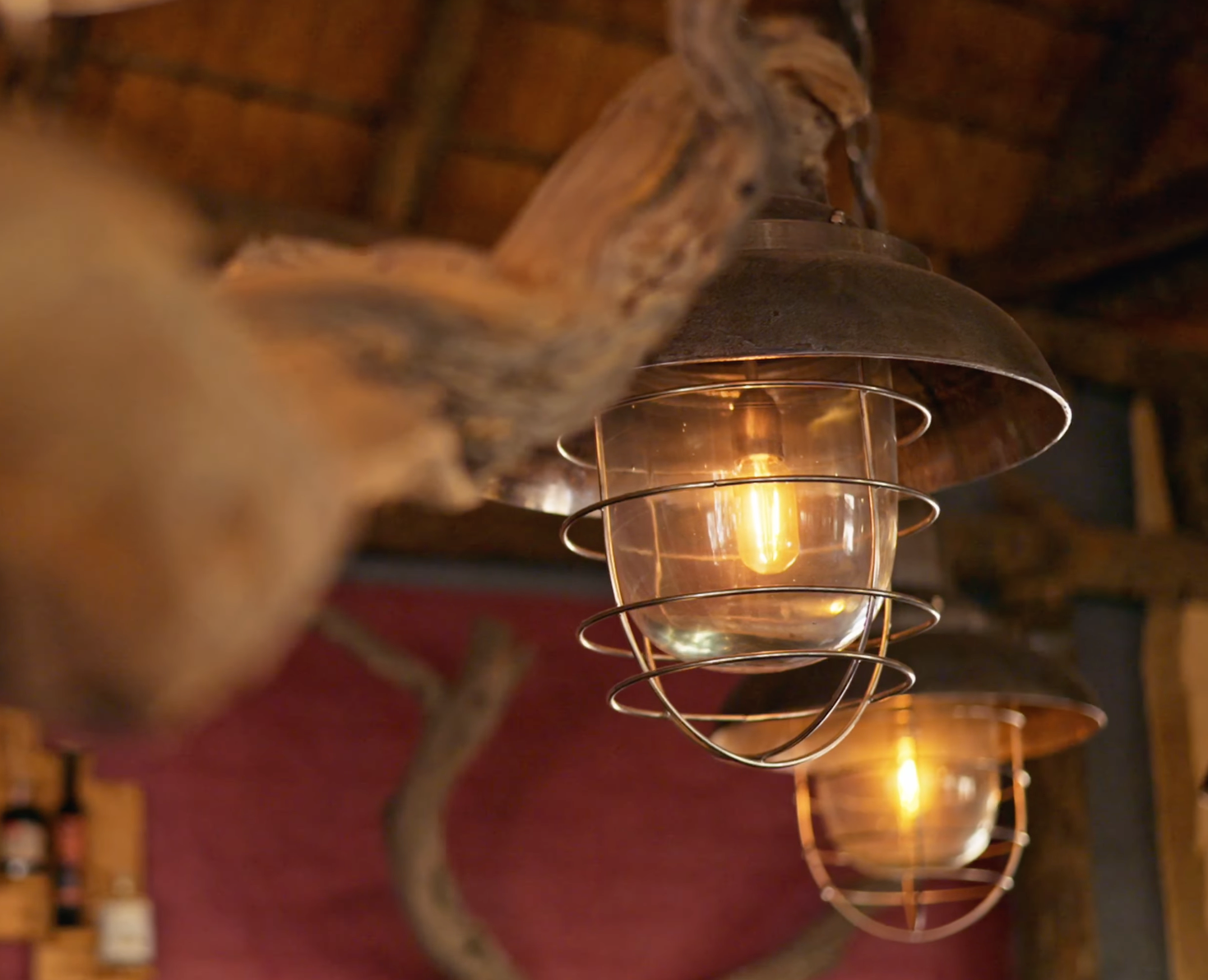 Vintage industrial cage pendant lights hanging from rustic wooden beam in a cozy restaurant setting.