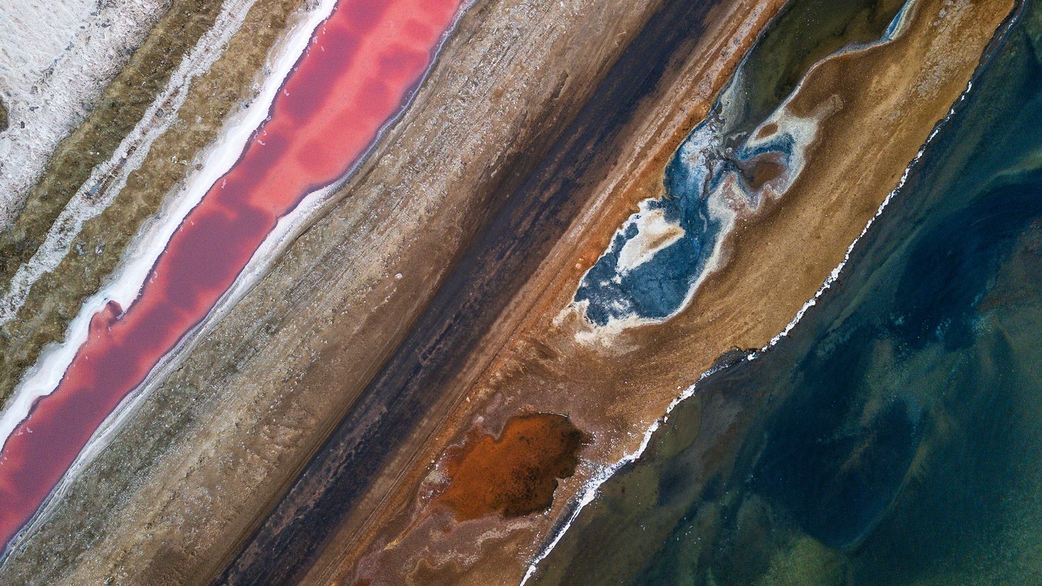 Aerial view of colorful salt flats with pink, orange, and teal water pools.