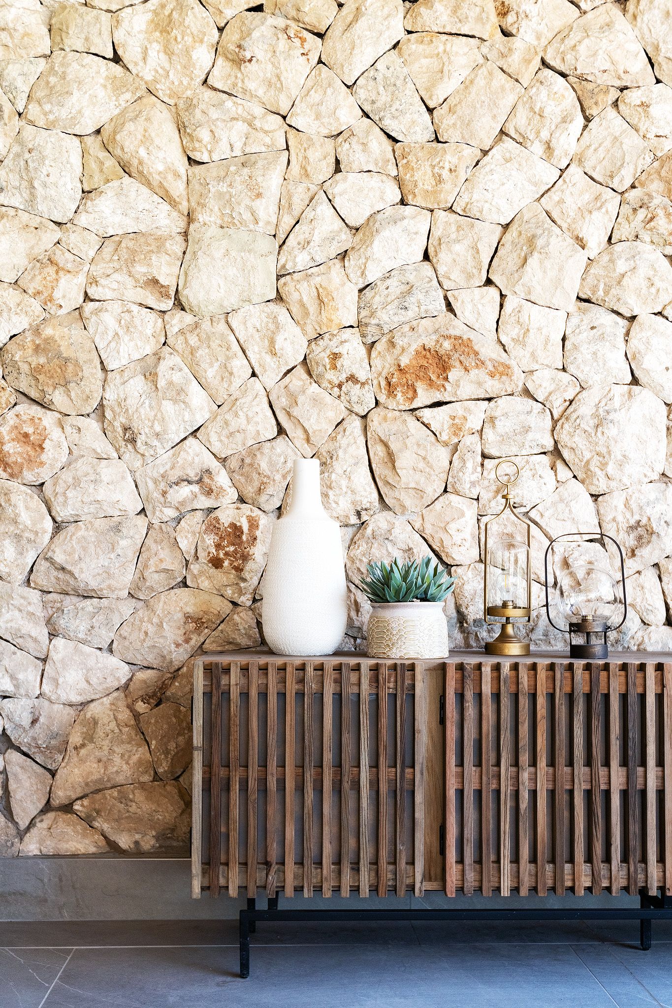 Rustic wooden sideboard with white vase, succulent, and candles against a natural stone wall.