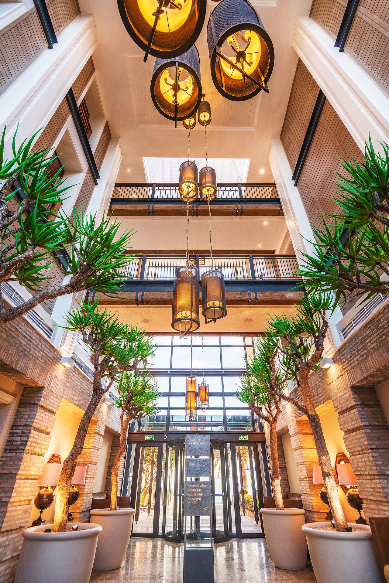 Elegant hotel lobby with tall ceilings, tropical trees, hanging lanterns, and a glass revolving entrance door.