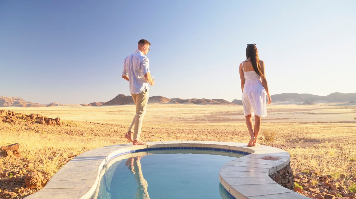 Couple standing by a luxury pool overlooking the vast Namib Desert landscape.