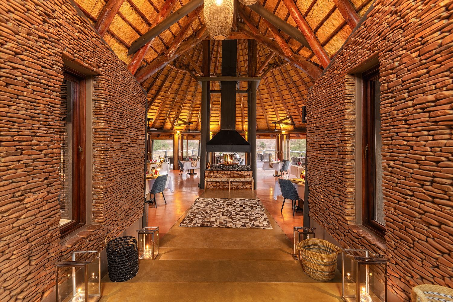 Dramatic stone-walled safari lodge entrance with thatched roof, fireplace, and lantern lighting.