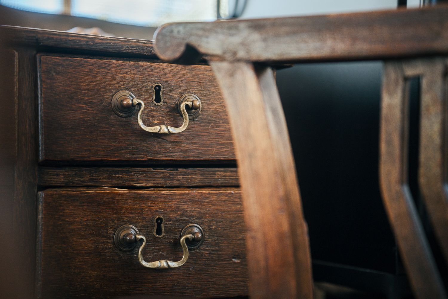 Close-up of antique wooden desk drawers with ornate brass keyhole escutcheons and drop bail handles.