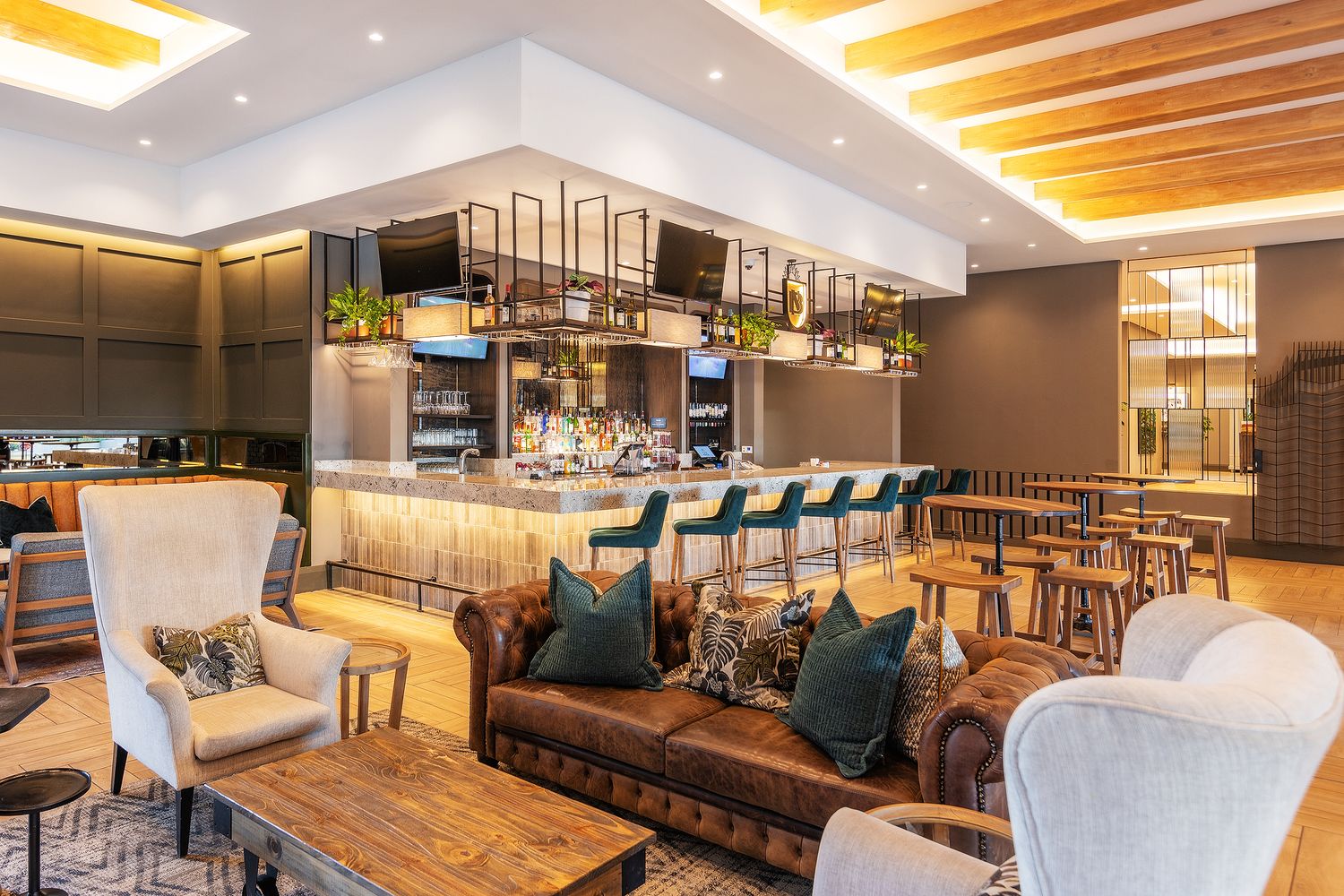 Modern hotel lounge bar featuring leather sofas, teal bar stools, warm lighting, and an elegant backlit bar counter.
