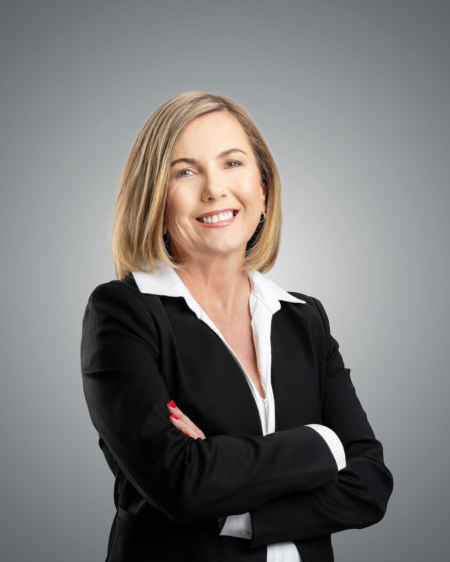 Professional woman in black blazer smiling confidently with arms crossed against gray background.