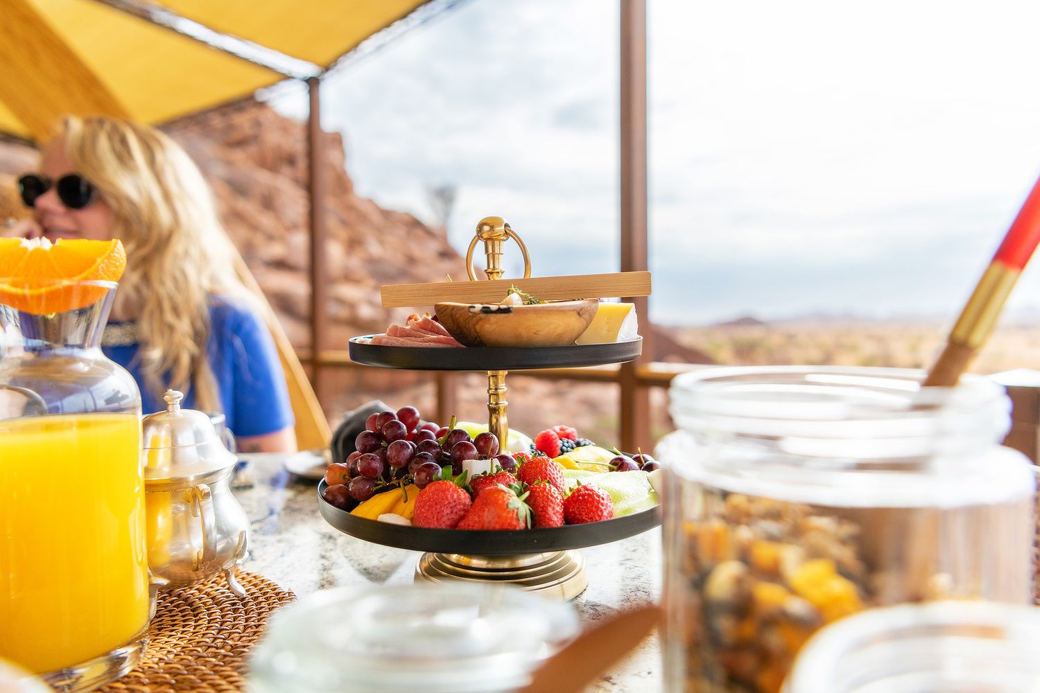 Elegant tiered fruit stand with fresh strawberries and grapes on a sunny outdoor table with orange juice.