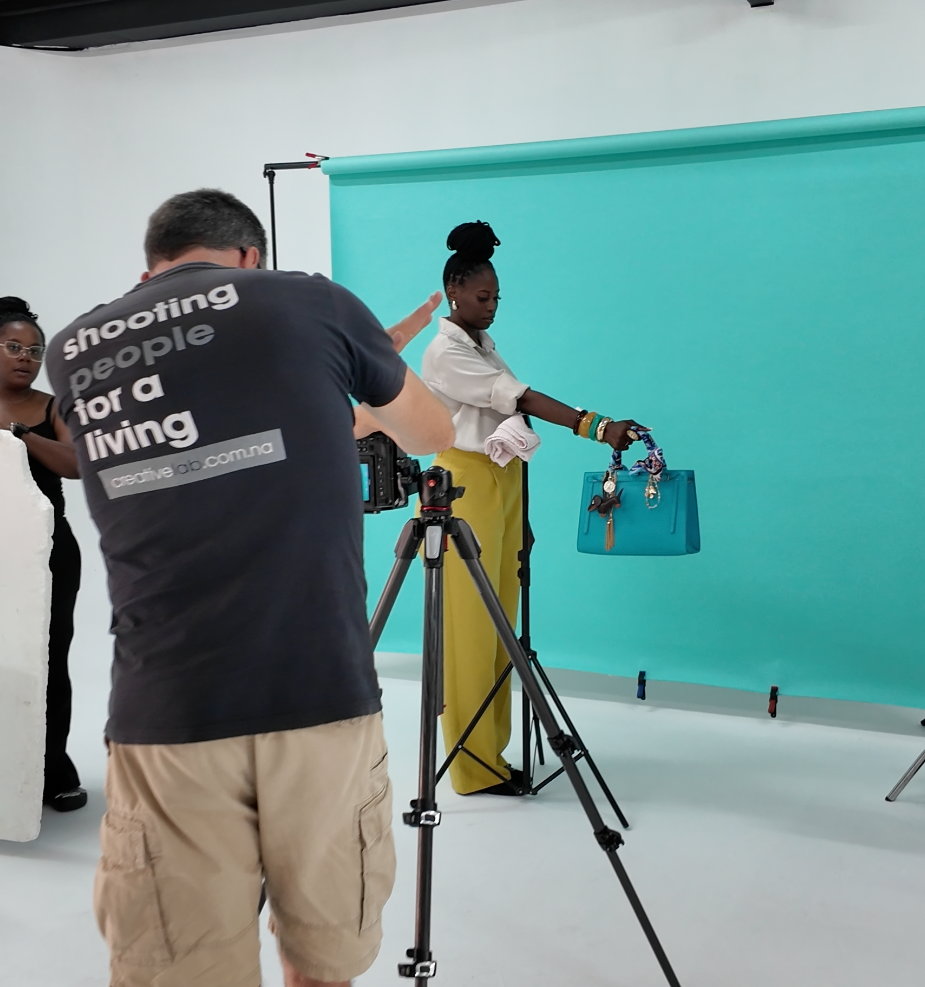 Photographer shooting a model holding a teal handbag against a turquoise backdrop in a professional studio.