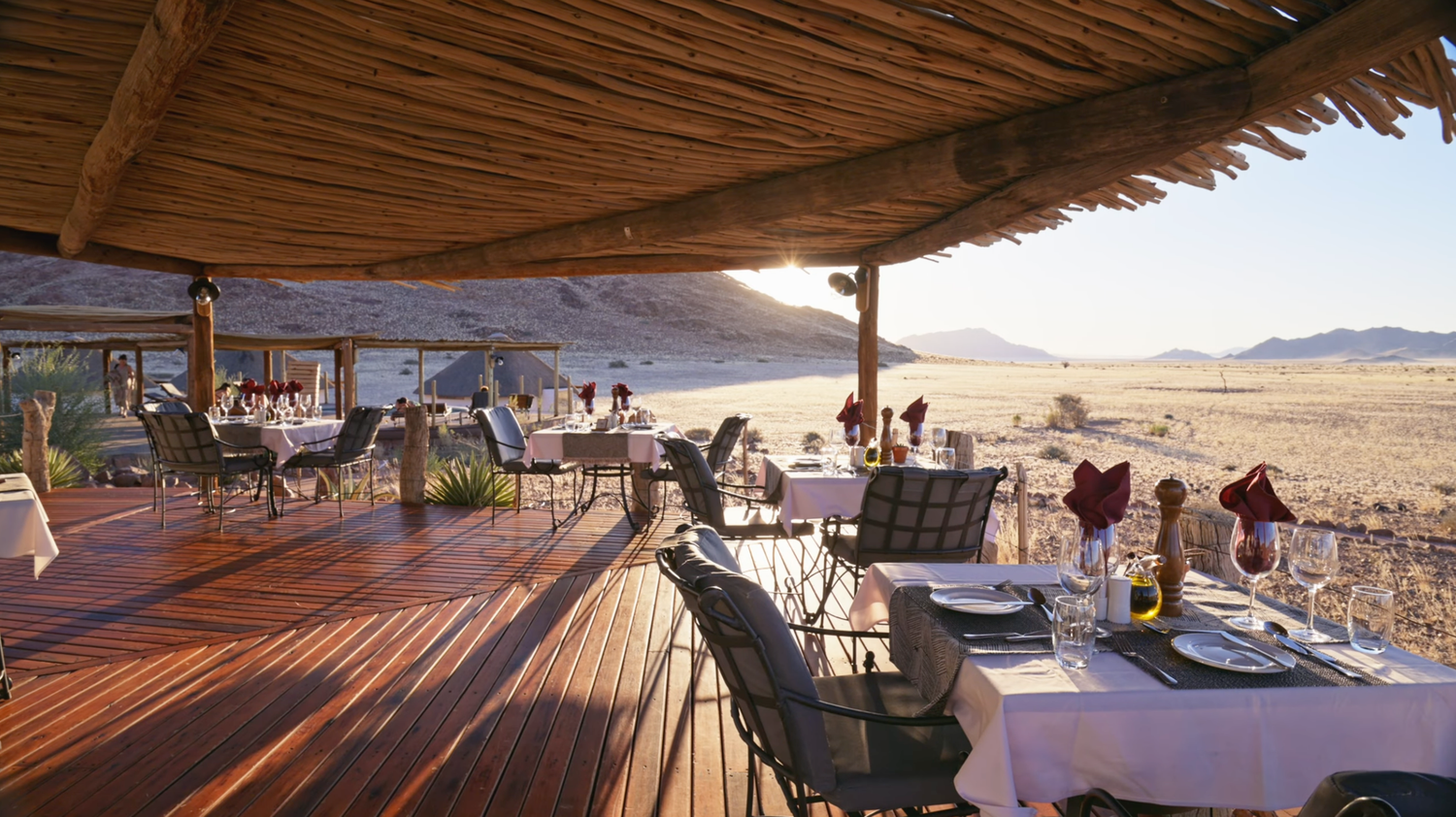 Elegant open-air safari lodge restaurant with thatched roof, wooden deck, and stunning desert landscape views.