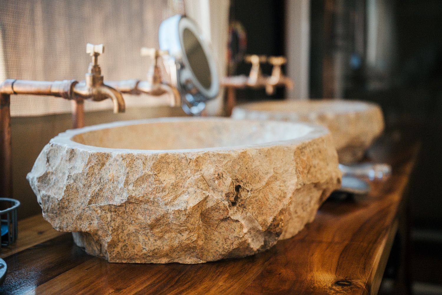 Rustic stone vessel sink on a wooden vanity with brass faucets in a stylish bathroom.