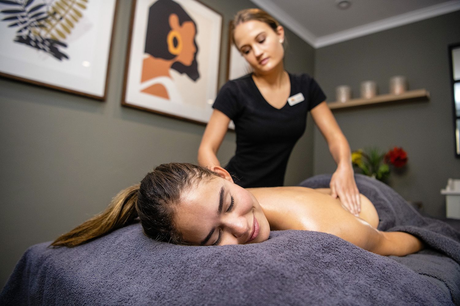 A massage therapist in black uniform performing a relaxing back massage on a client at a spa.