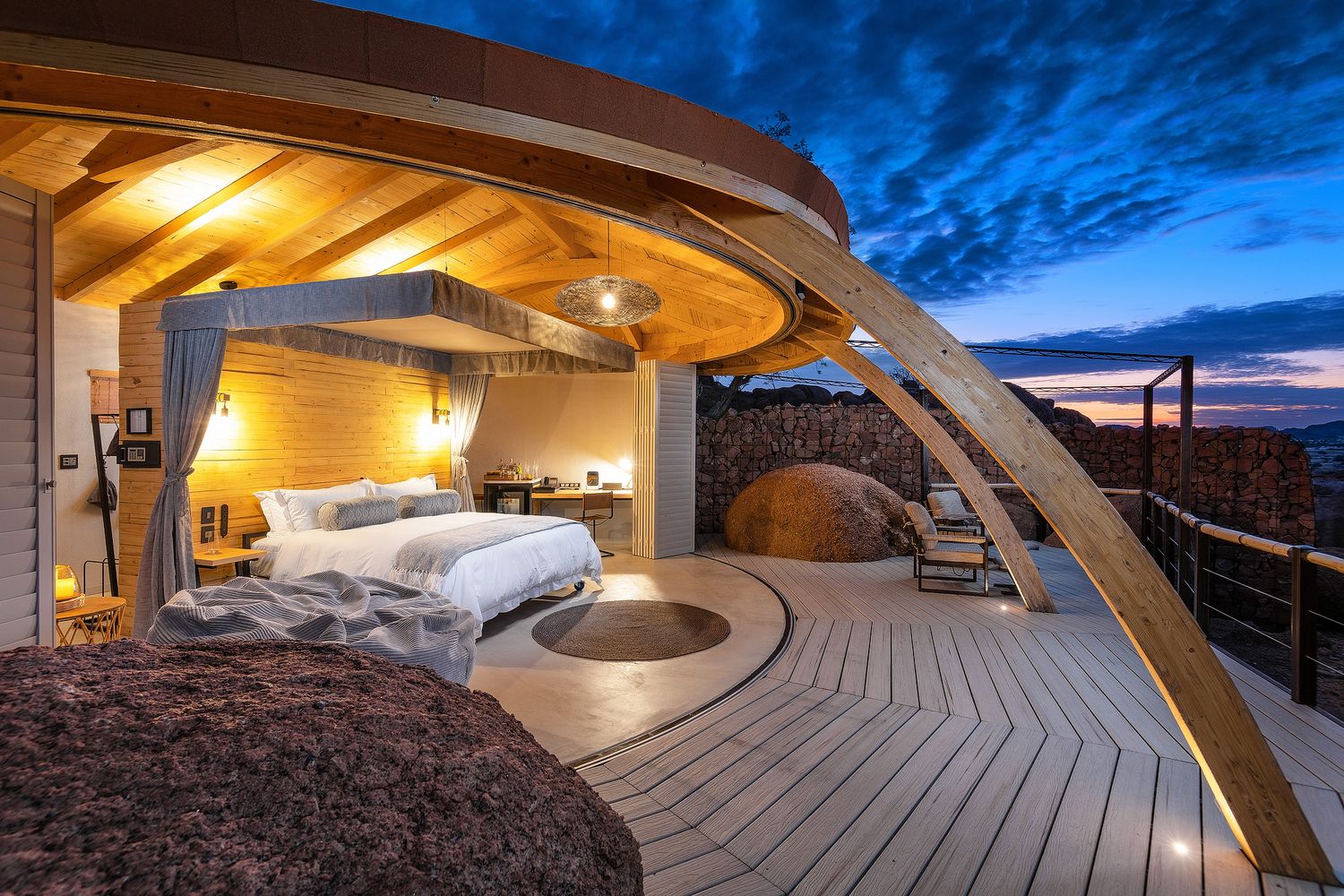 Stunning open-air luxury tent suite with wooden curved roof, king bed, and breathtaking twilight sky views.