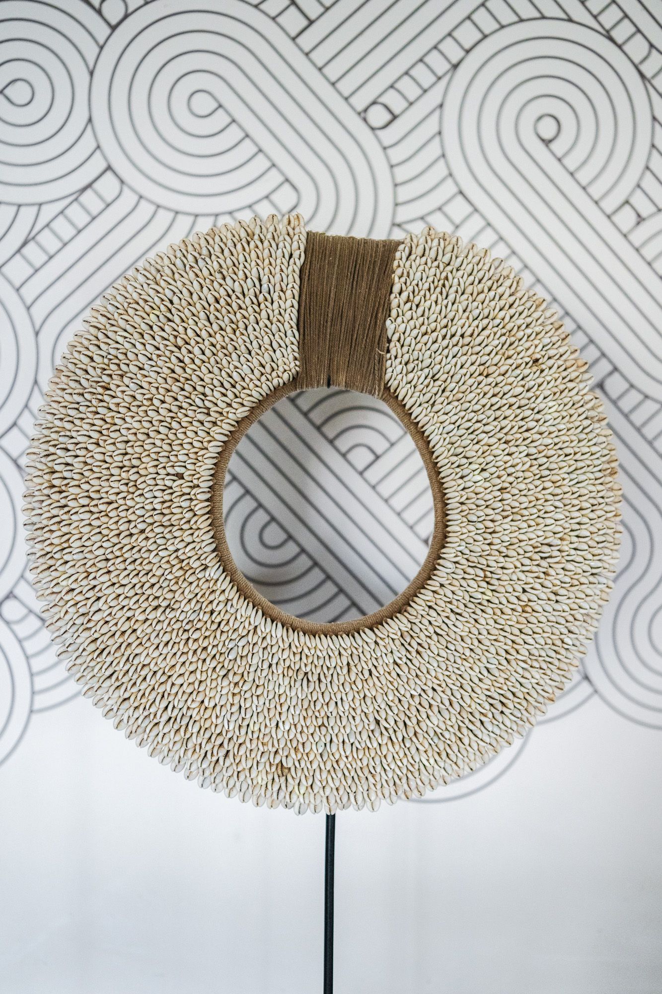 Decorative round woven shell wall art with jute accent on geometric patterned white background.
