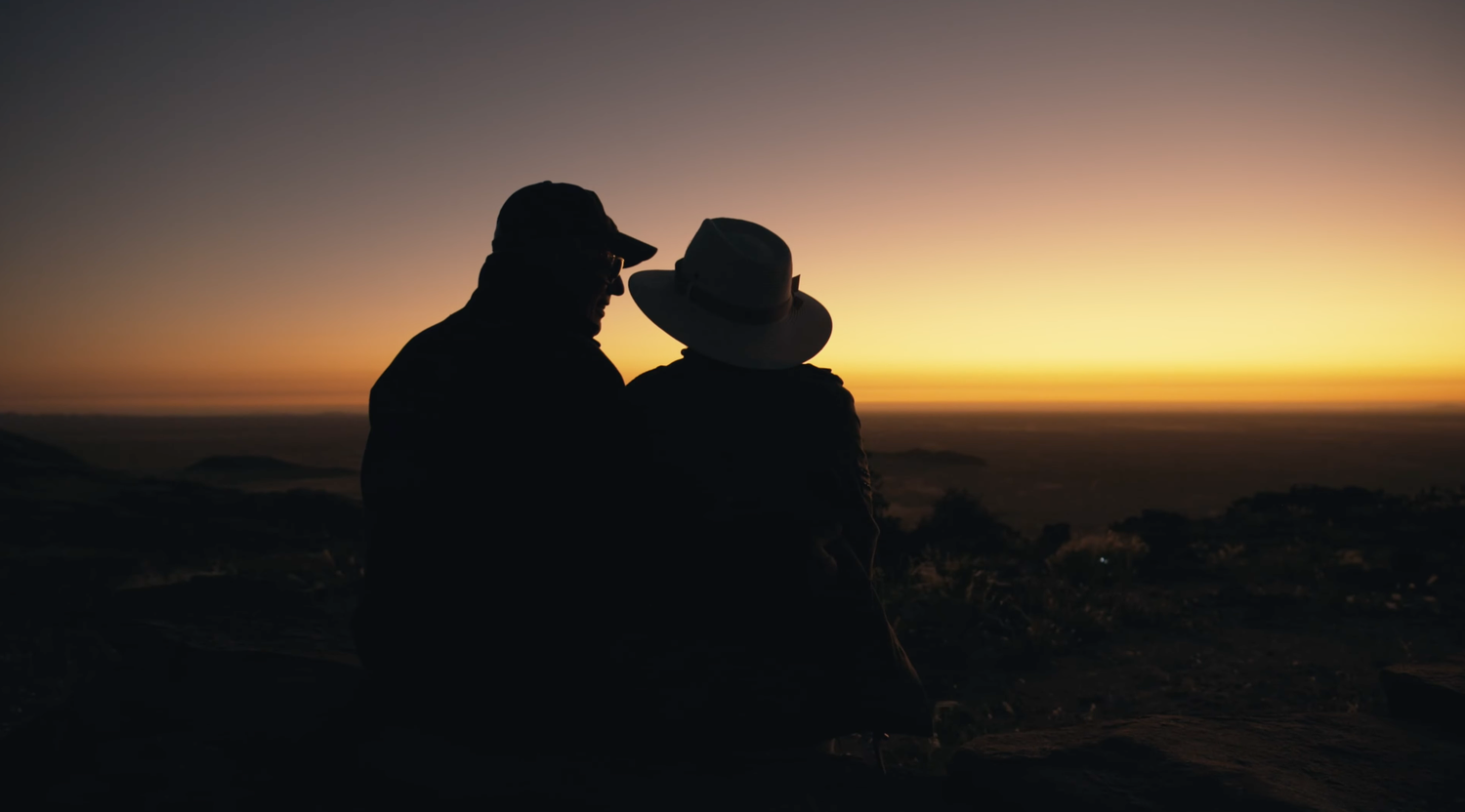Romantic couple silhouetted against a golden sunset sky, sharing an intimate moment on a hilltop overlook.