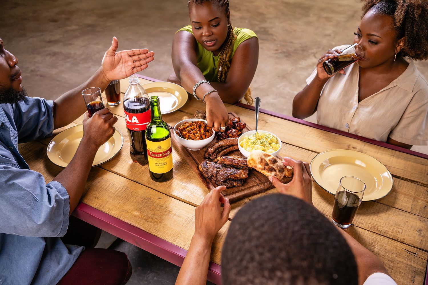 Friends sharing a BBQ meal with ribs, beans, and drinks at a wooden table in a casual outdoor restaurant.
