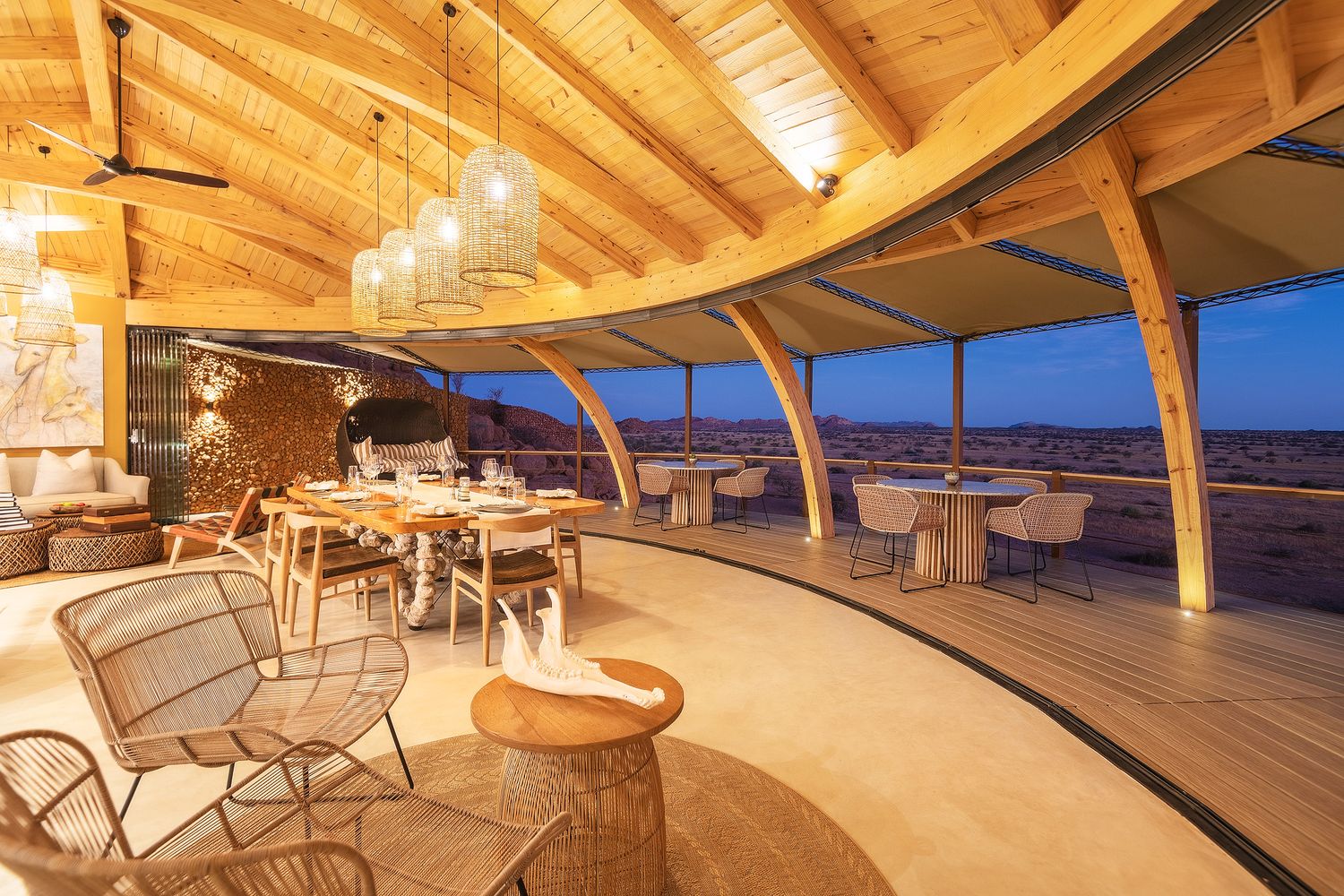 Curved wooden beamed ceiling restaurant at a luxury desert lodge with wicker chairs and sweeping open-air views.