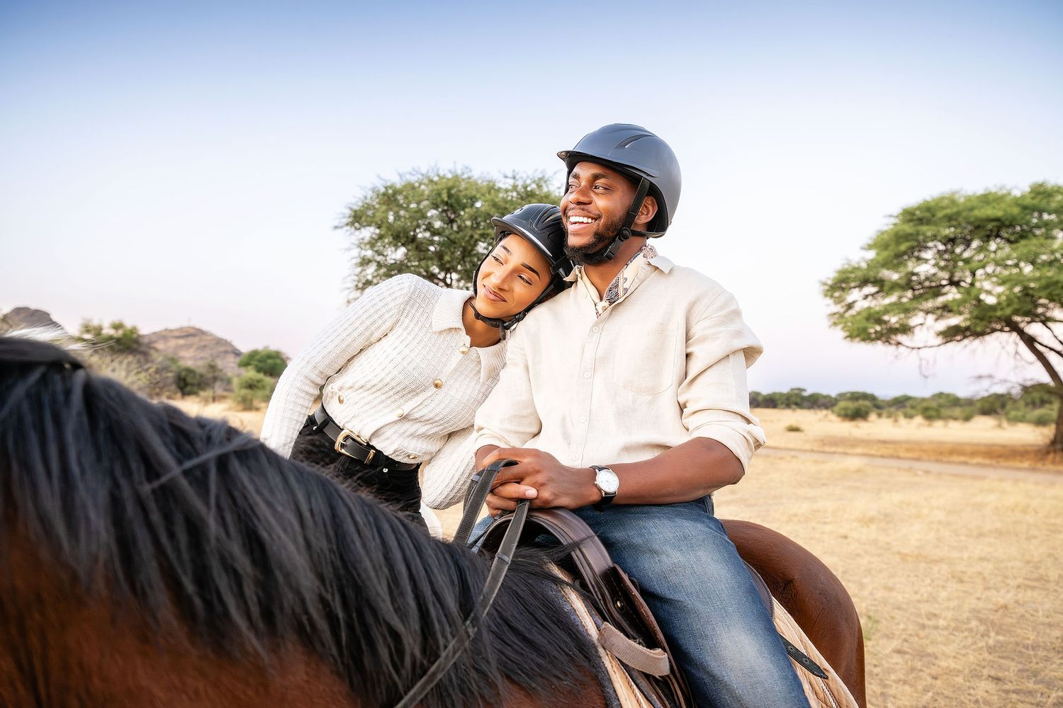 A happy couple rides a horse together through a scenic African savanna landscape on a sunny day.