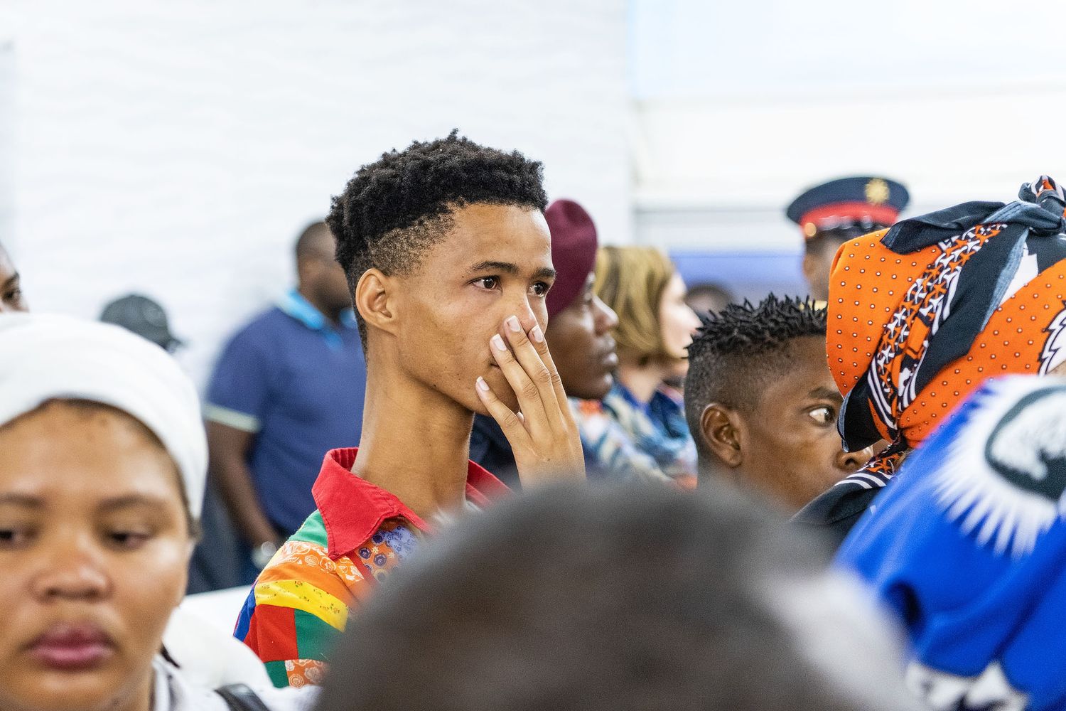 Young man covering his mouth in a crowd of people at a cultural gathering event.