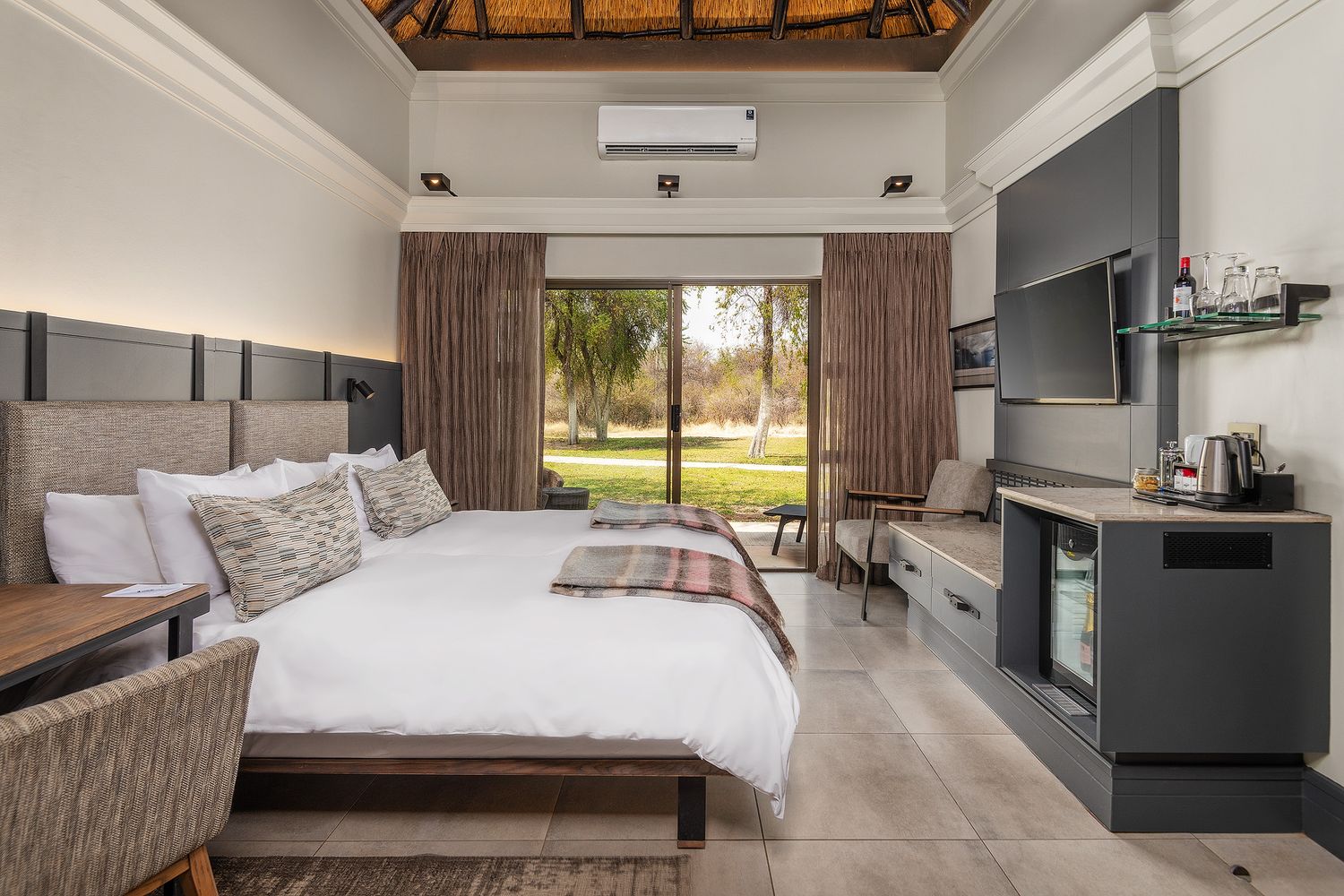 Spacious luxury safari lodge bedroom with king bed, garden view, thatched ceiling, and modern amenities.