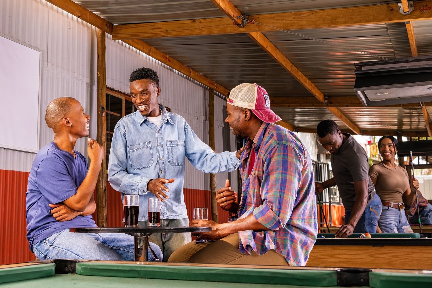 Friends shaking hands at an outdoor bar, sharing drinks and enjoying a social gathering near a pool table.
