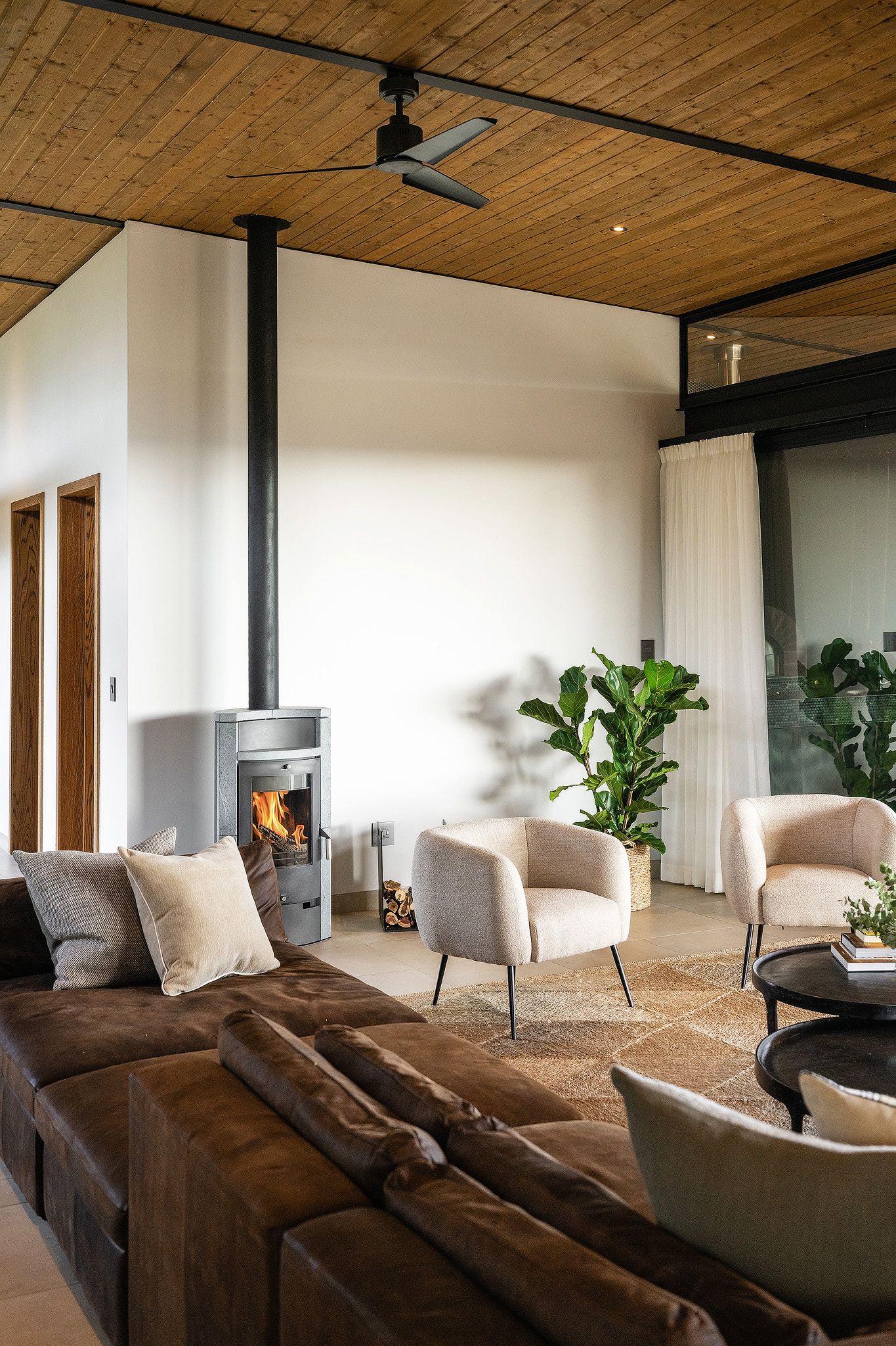 Cozy living room with wood-burning fireplace, leather sofa, cream armchairs, and wooden ceiling.