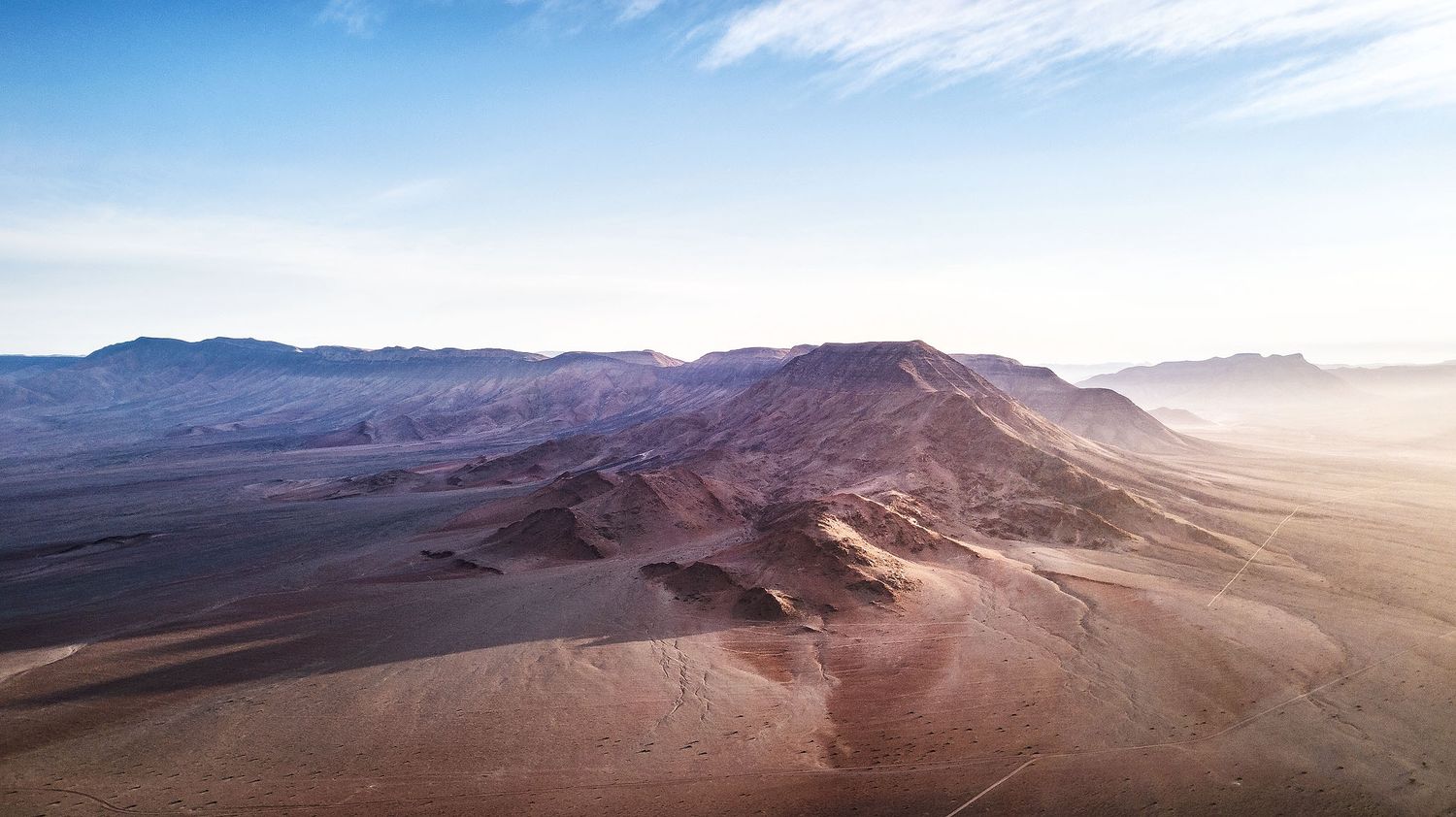 Aerial view of vast desert landscape with sandy dunes and mountains under a hazy sky.