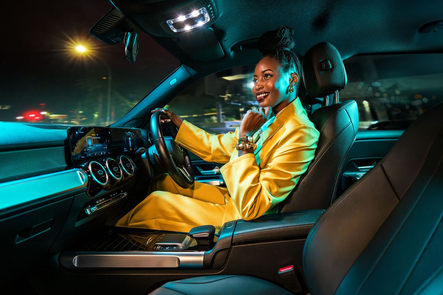 A smiling woman in a yellow suit sits in a luxury car at night, illuminated by teal ambient lighting. FNB