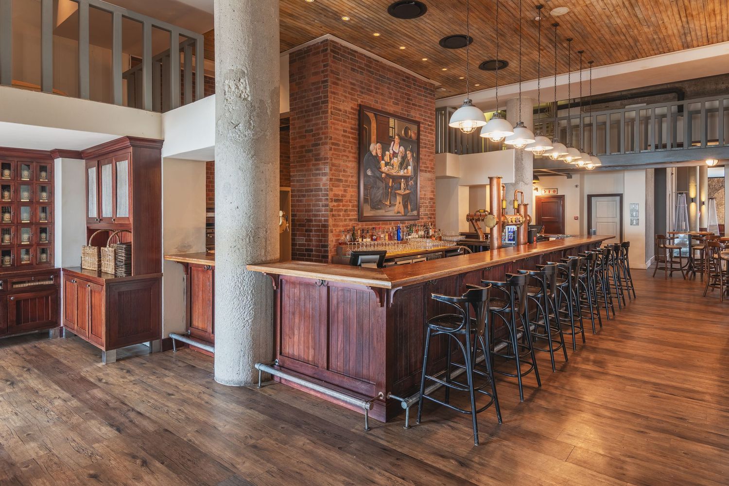 Rustic bar with long wooden counter, black stools, brick accents, and hardwood floors in an upscale restaurant interior.