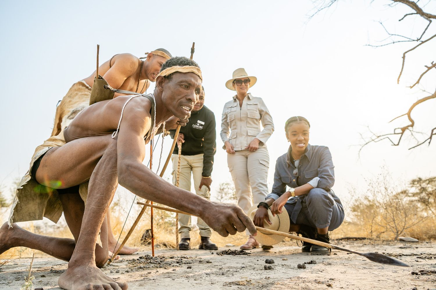 San Bushmen demonstrate traditional fire-making techniques to fascinated tourists in the African wilderness.
