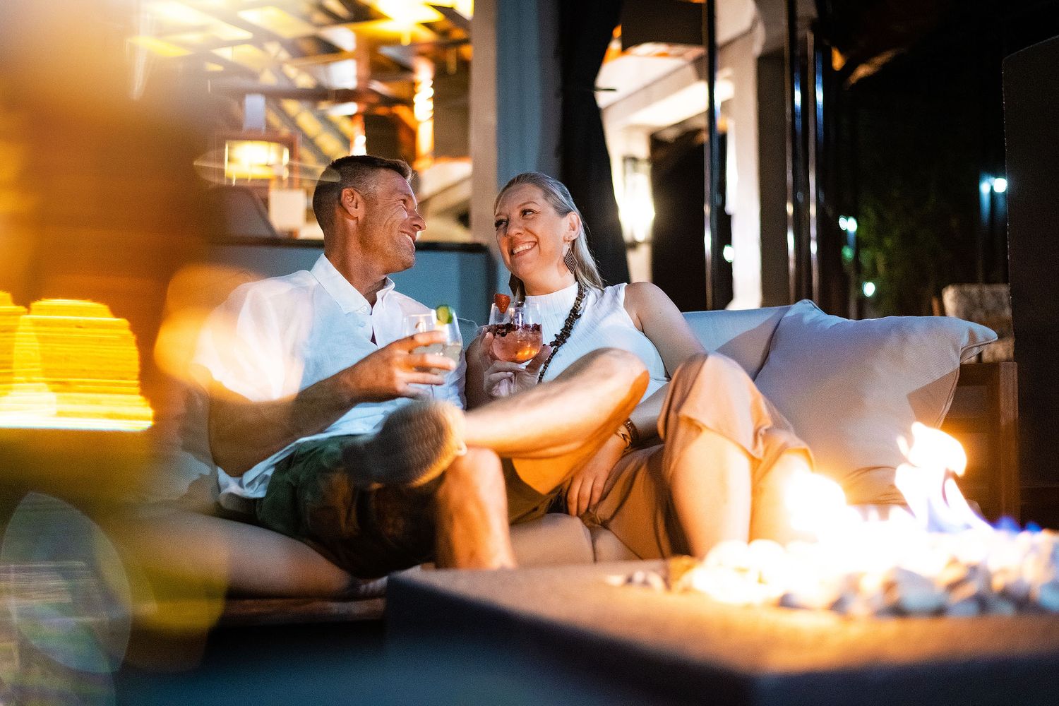 Couple relaxing by a fire pit at night enjoying drinks at a luxury African safari lodge.
