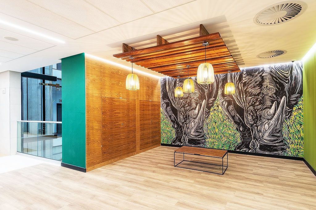 Modern office lobby with dramatic rhino mural, wooden slat ceiling, pendant lights, and teal accent wall.